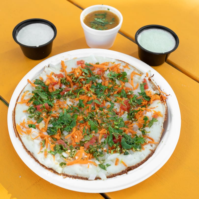 Savory uttapam pancake topped with carrots, onions, tomatoes, and cilantro, served with three dipping sauces.