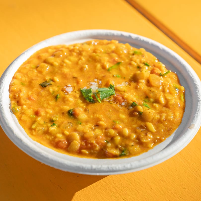 Close-up of a white bowl filled with a rich orange lentil stew, garnished with fresh herbs.