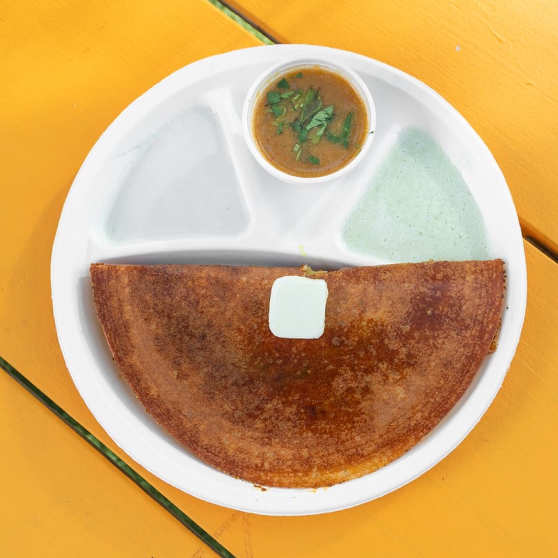 A crispy brown dosa with a pat of butter, served with two chutneys and sambar on a white plate.