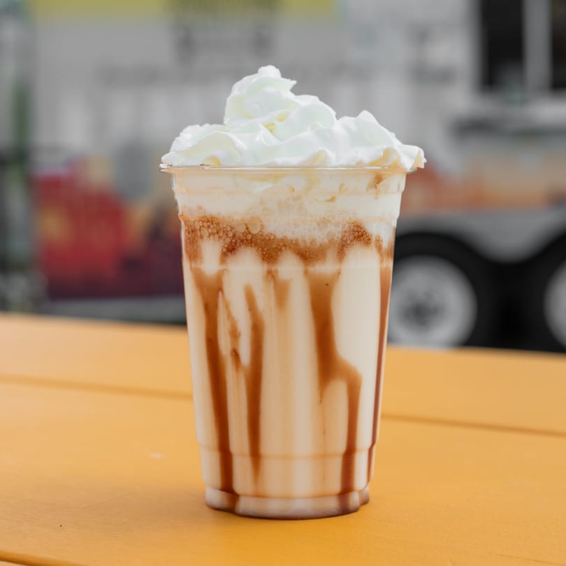 A milkshake with chocolate syrup and whipped cream sits on a bright orange table.
